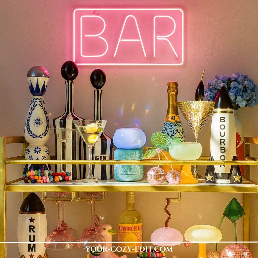 gold bar cart styled with a glowing pink neon BAR sign on the wall, colorful liquor bottles, striped decanters, blue hydrangea flowers, and fun cocktail glasses